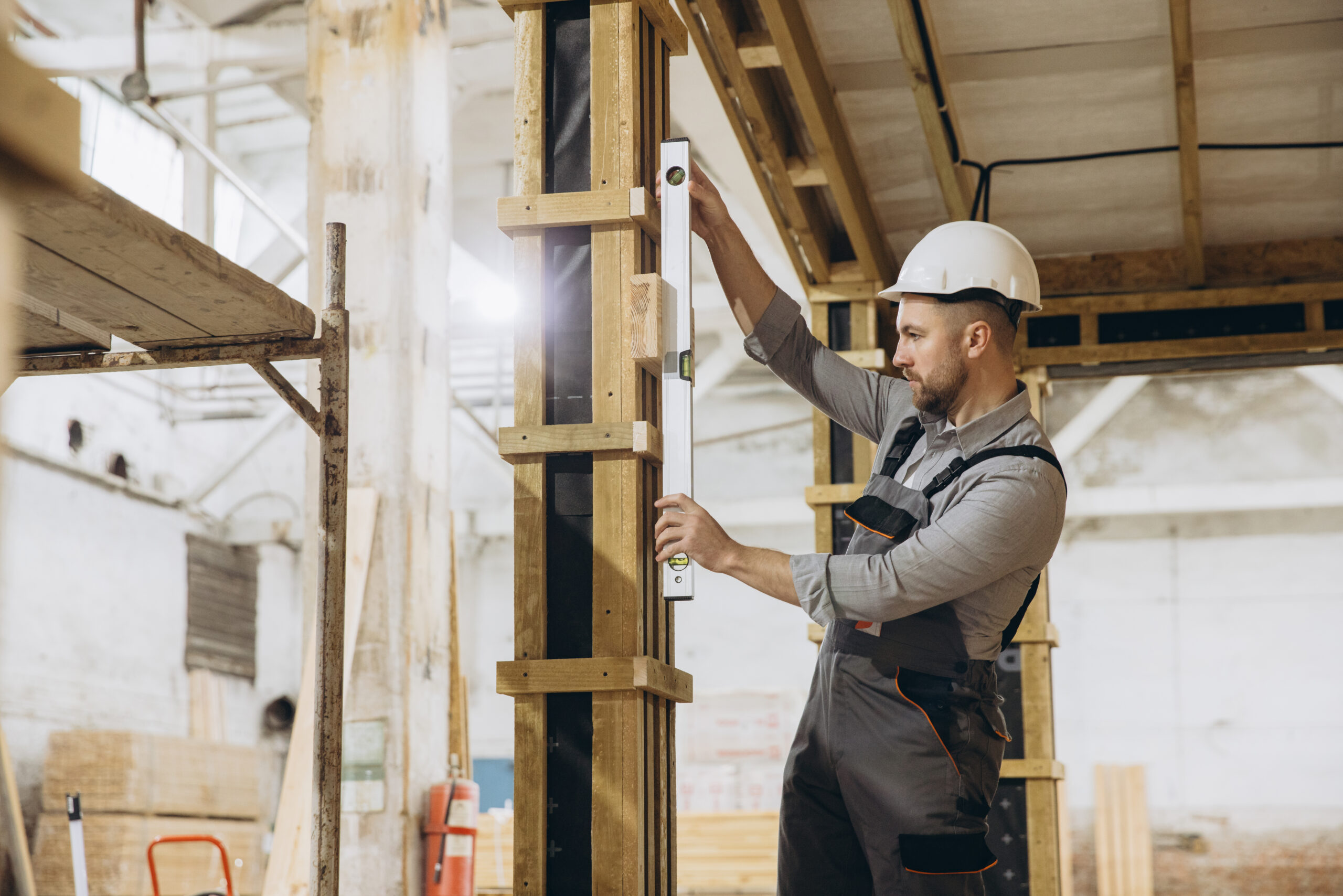 Construction worker using spirit level ensuring vertical alignment of support beam during modular building construction
